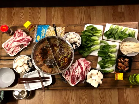 A hot pot spread with sliced meat, greens and mushrooms around a split pot