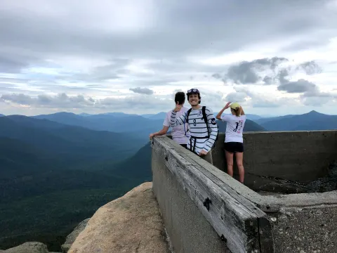 Three hikers at a stone lookout above forested mountains